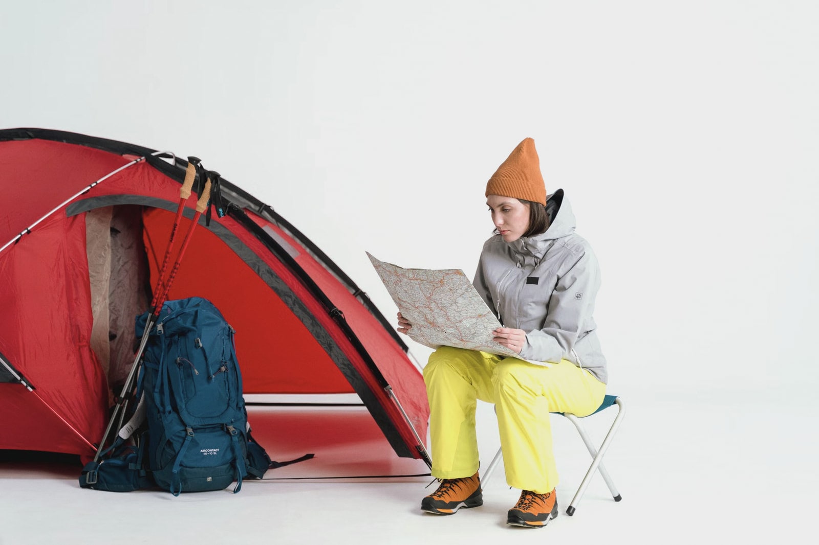 A traveler in cold-weather clothing studying a paper map beside a red tent and backpack