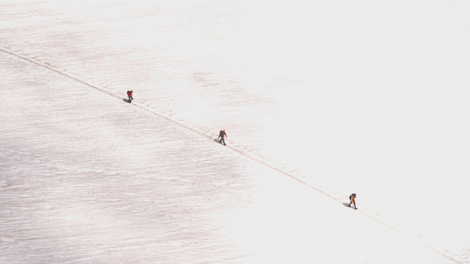 Three climbers following a track across a high, snow-covered ridge
