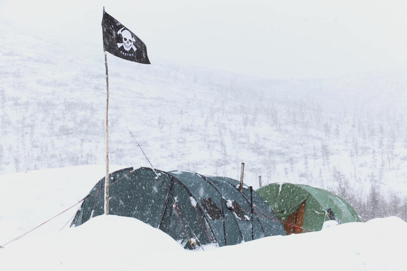Expedition tents half-buried in drifting snow during a storm
