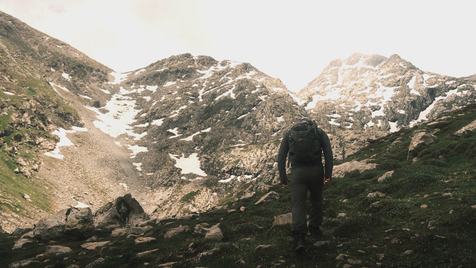 A hiker with a backpack walking toward rocky peaks streaked with snow
