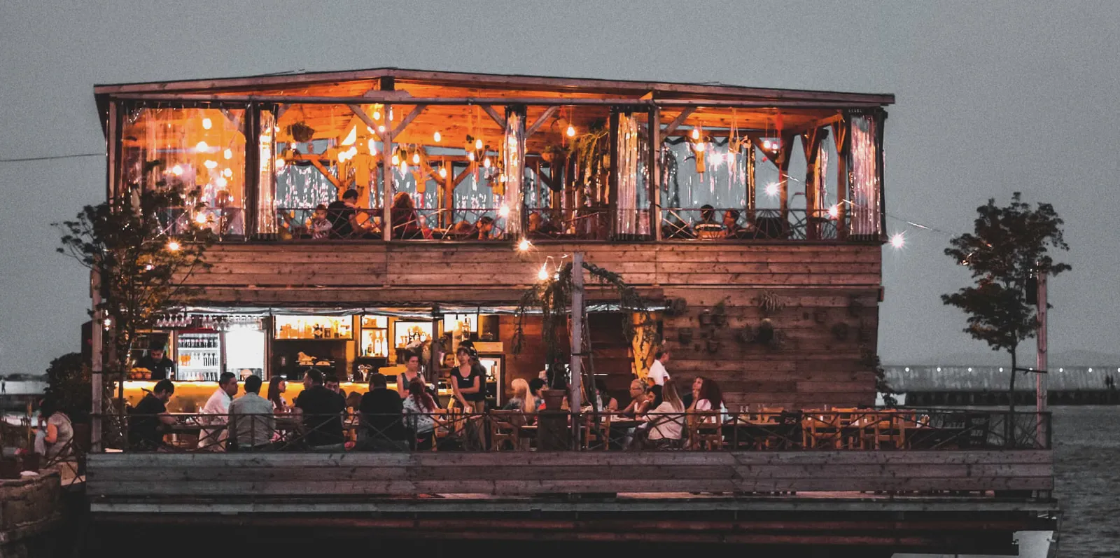 Гости ужинают в деревянном ресторане у воды